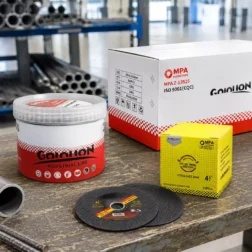 Discos de corte ultrafinos de 105 mm y cartón al por mayor colocados en un banco de trabajo de fabricación de metales con barras de acero, mostrando la capacidad de profundidad de corte adicional para procesamiento industrial.